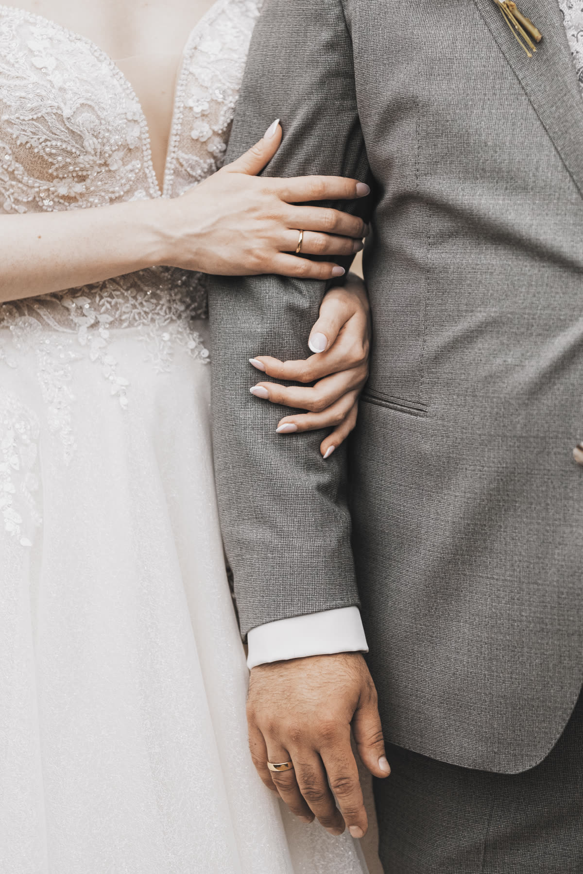 Detailaufnahme: Braut hält den Arm ihres Bräutigams, Hochzeitskleid mit Spitzenapplikation im Fokus